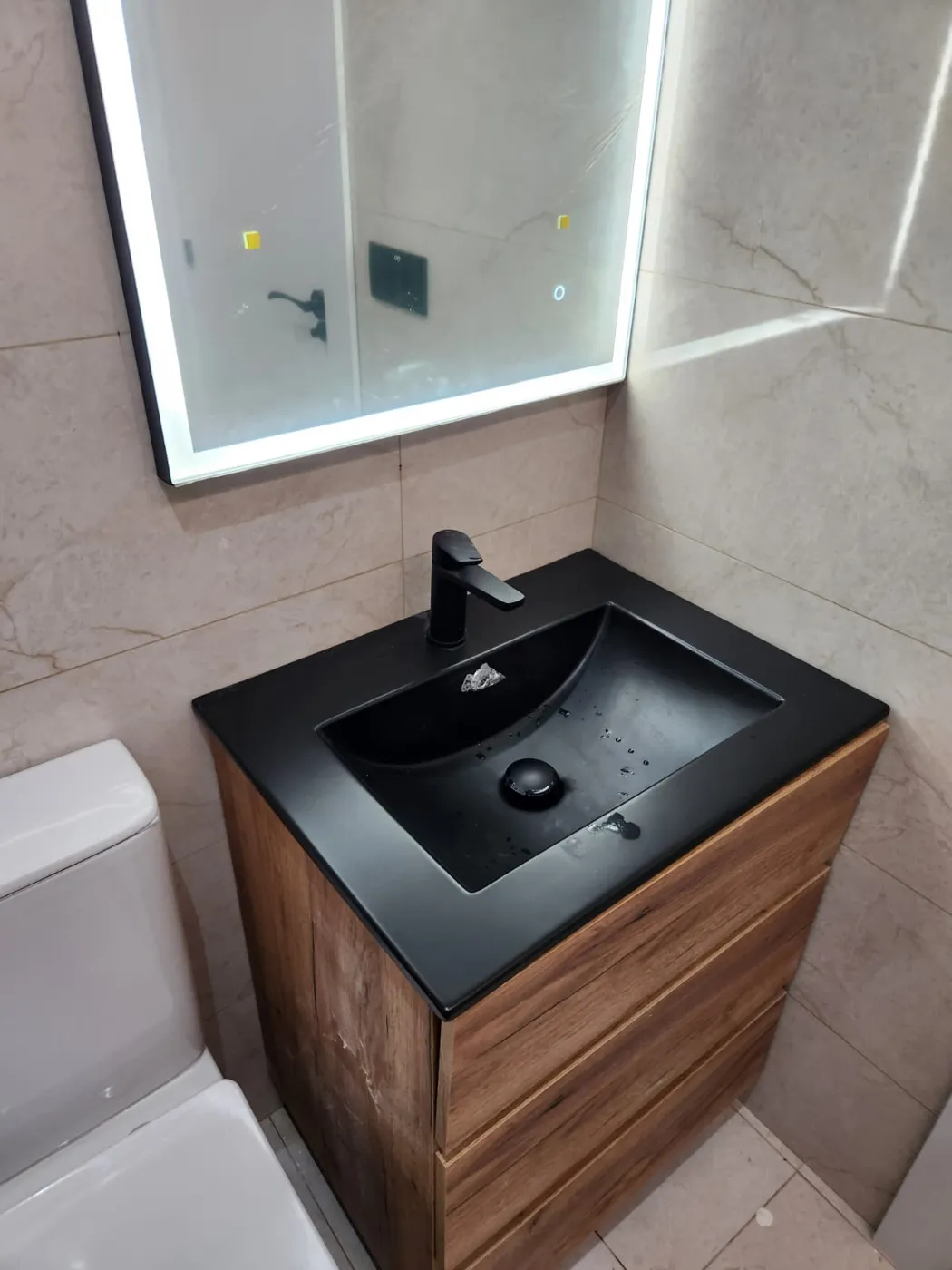Detalle de lavabo negro sobre mueble de madera y espejo retroiluminado