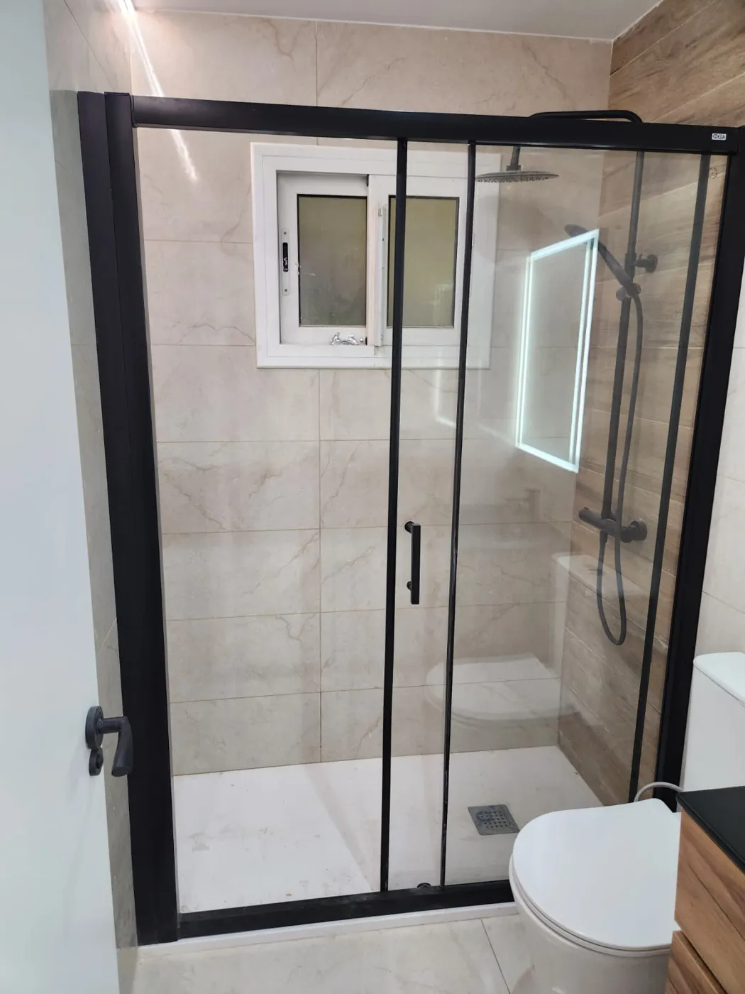 Ducha con mampara corredera negra y revestimiento porcelánico