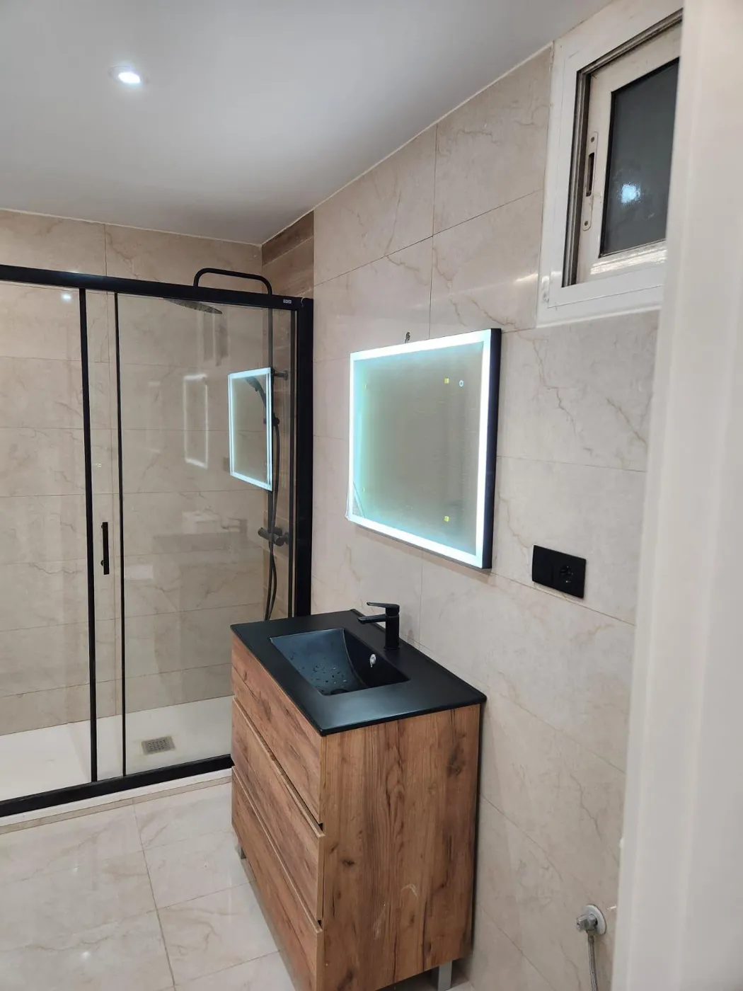 Baño completo reformado con ducha, mueble de madera y espejo LED